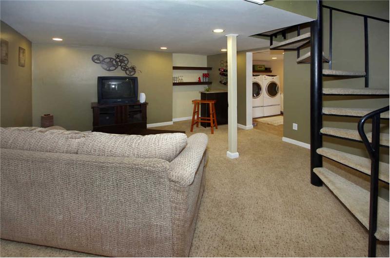 Spiral staircase leads down to family room in the finsihed basement with recess lighting throughout