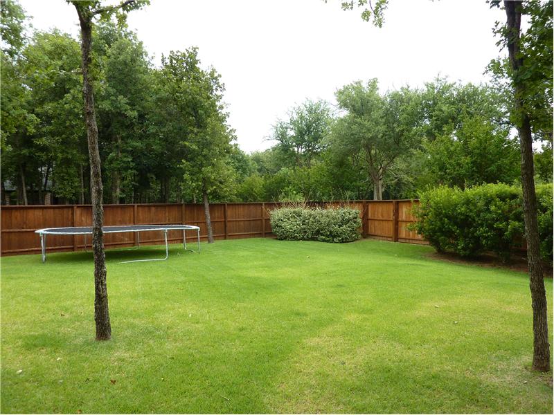 The large backyard is treed and surrounded by a  wood fence.